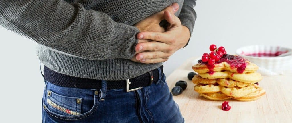 man with poor gut health holding stomach standing next to a stack of pancakes with berries on top