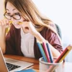 A stressed woman looking at her computer and biting a pencil needs ways to relieve stress